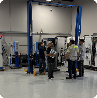 Instructors mentoring students beside vehicle hoist